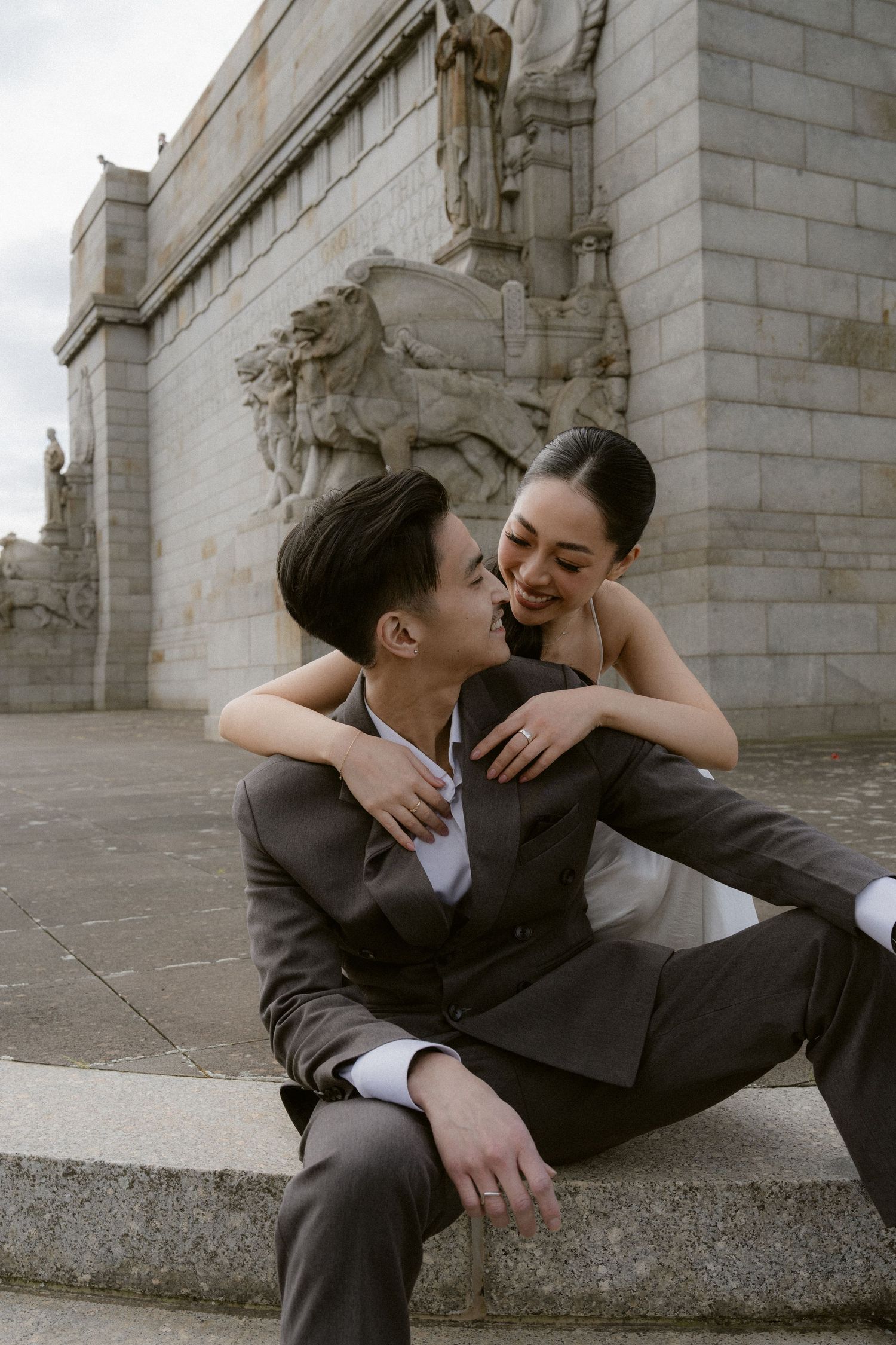 Couple in elegant wedding attire sharing a romantic moment on stone steps before a classical monument.