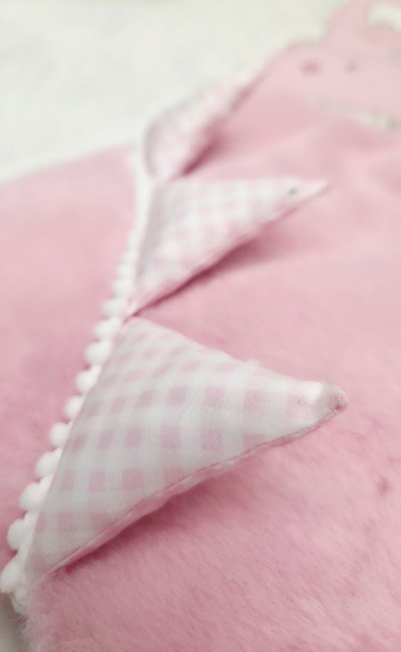 Close-up of pink fleece fabric with gingham check trim and white picot lace edging detail.
