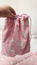 Pink drawstring bag featuring cute white llama and floral print pattern, held open to show interior capacity.