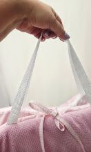Pink waffle tote bag with white ribbon handles held by hand, soft pastel design.