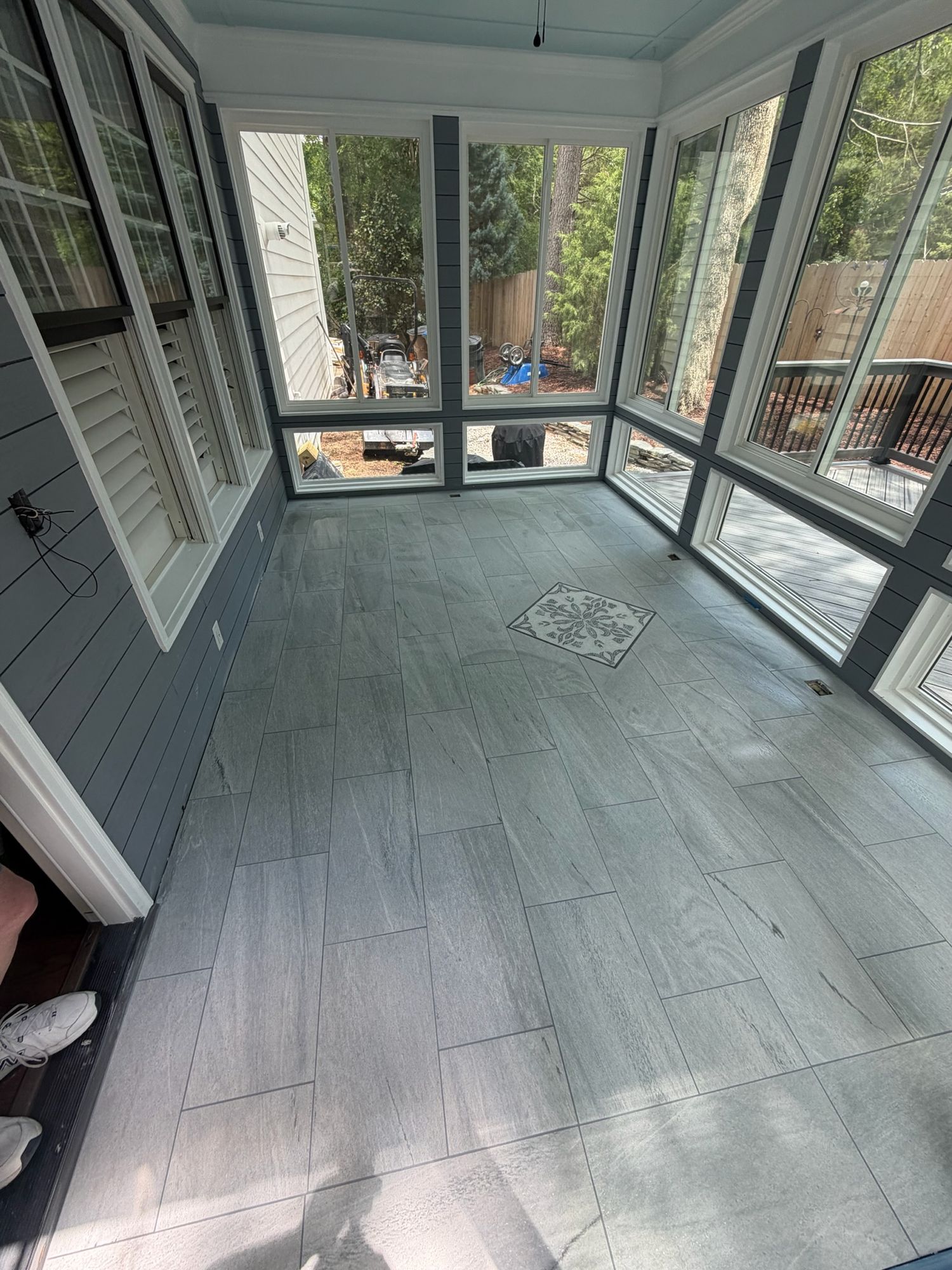 Spacious screened porch with gray large-format tile flooring and decorative center medallion.