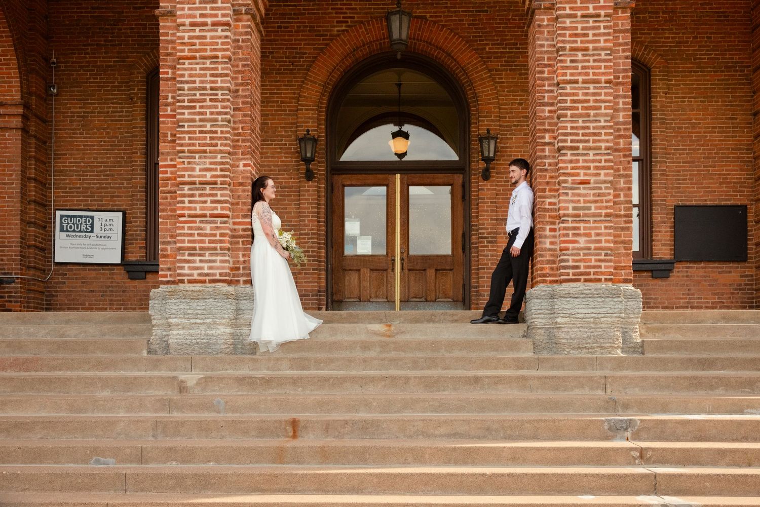 Bride and groom stand apart on brick church steps, facing each other in a romantic wedding portrait.