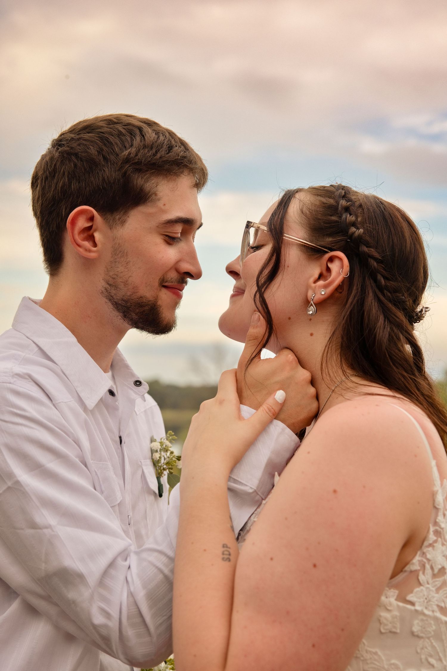 A groom tenderly holds his bride's face as they share an intimate moment outdoors on their wedding day.