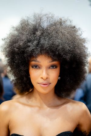 Close-up portrait of a woman with a voluminous natural afro hairstyle, wearing a strapless top outdoors.