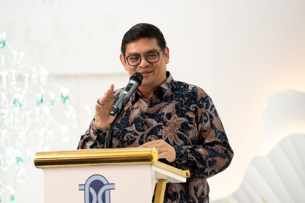 Man in batik shirt speaking at podium during formal event.