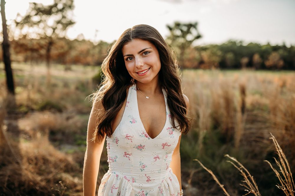 Young woman in floral sundress smiling outdoors in golden field during sunset.