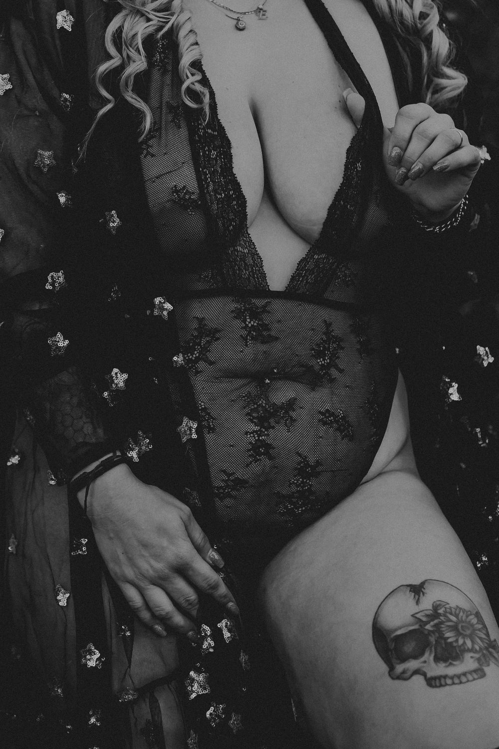 Black and white photo of a woman in lace lingerie and floral robe, featuring a skull tattoo on her thigh.