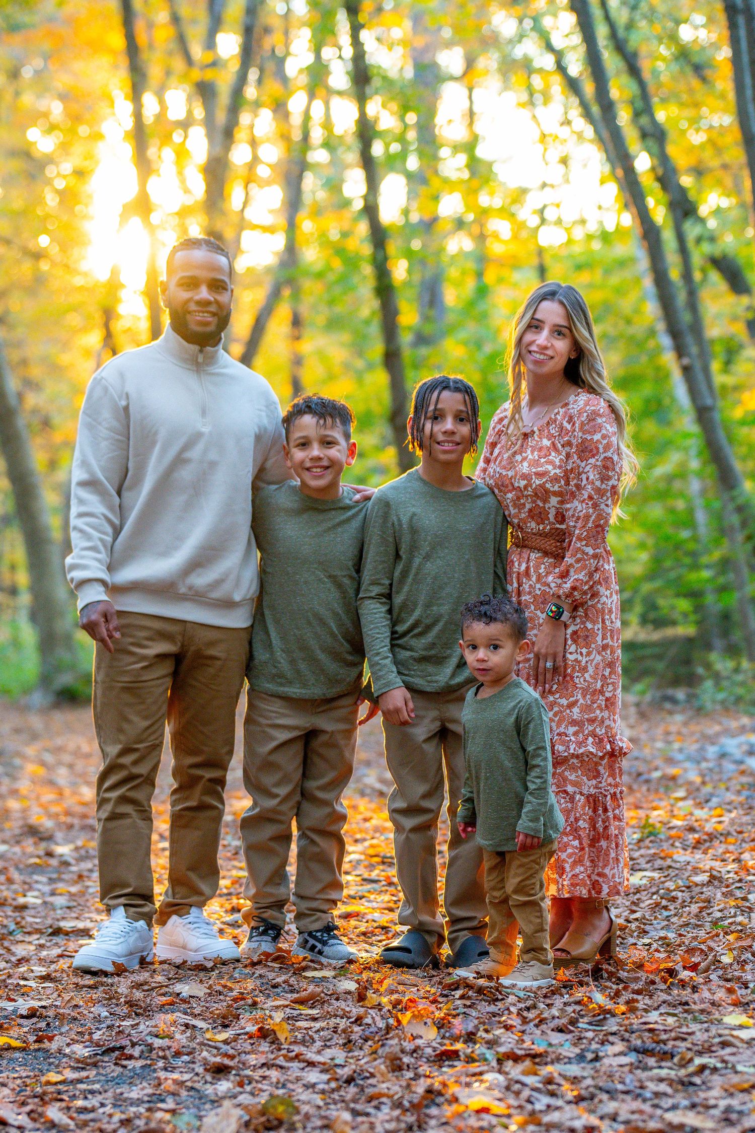 Family of five posing in autumn forest with golden sunlight filtering through colorful fall foliage.