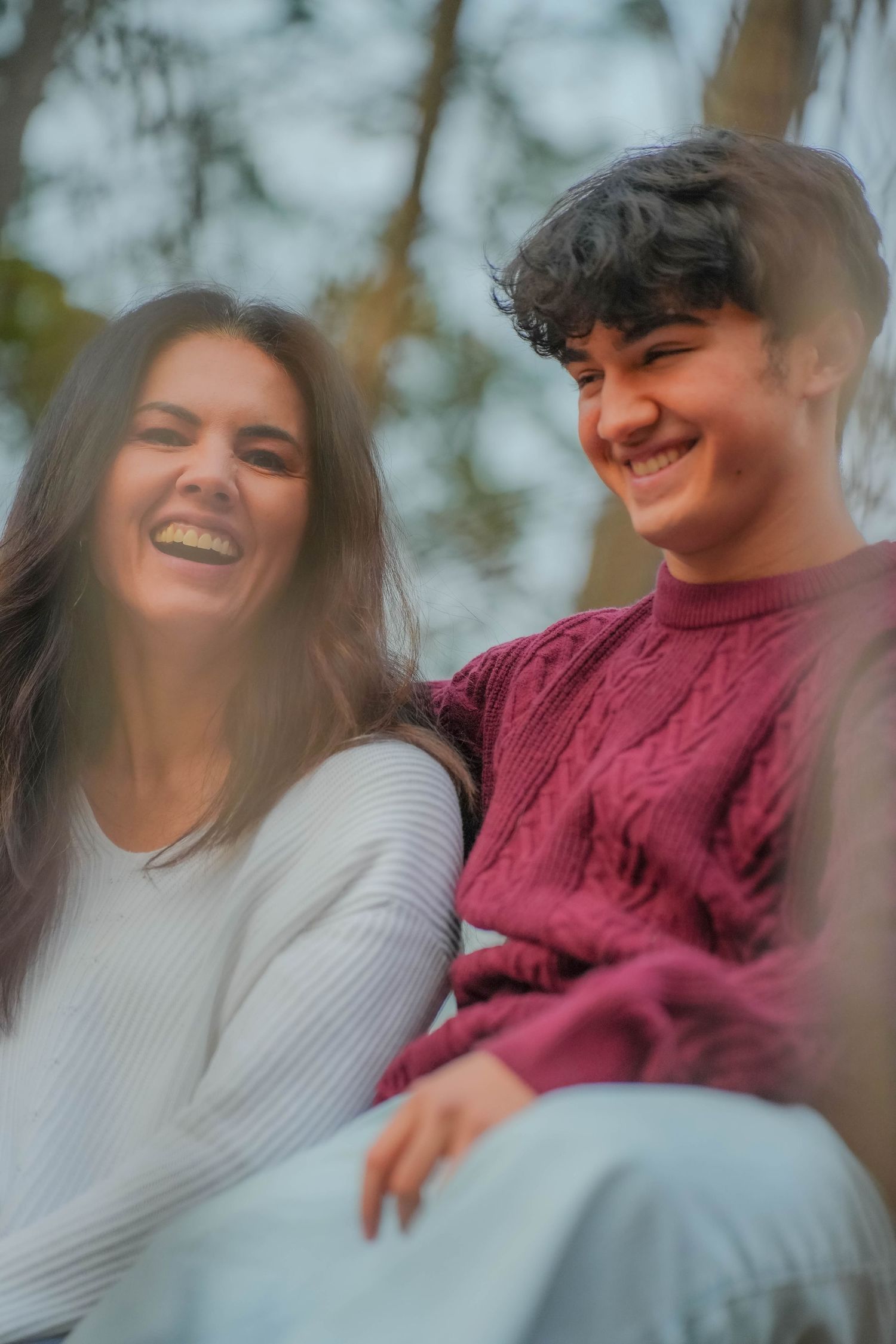 Two young people smiling and laughing together outdoors, wearing cozy sweaters in a candid, joyful moment.