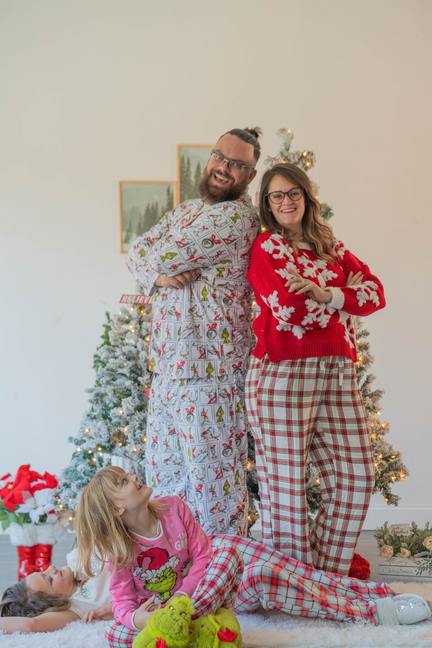 Family in festive Christmas pajamas posing by decorated tree with young child sitting on floor.