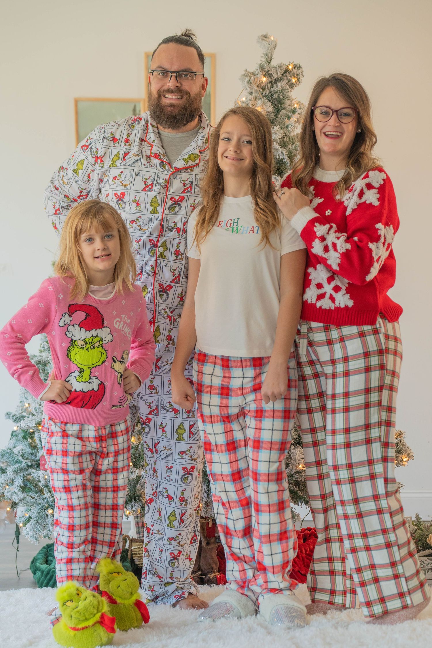 Family of four posing in Christmas pajamas and holiday sweaters in front of a decorated tree.