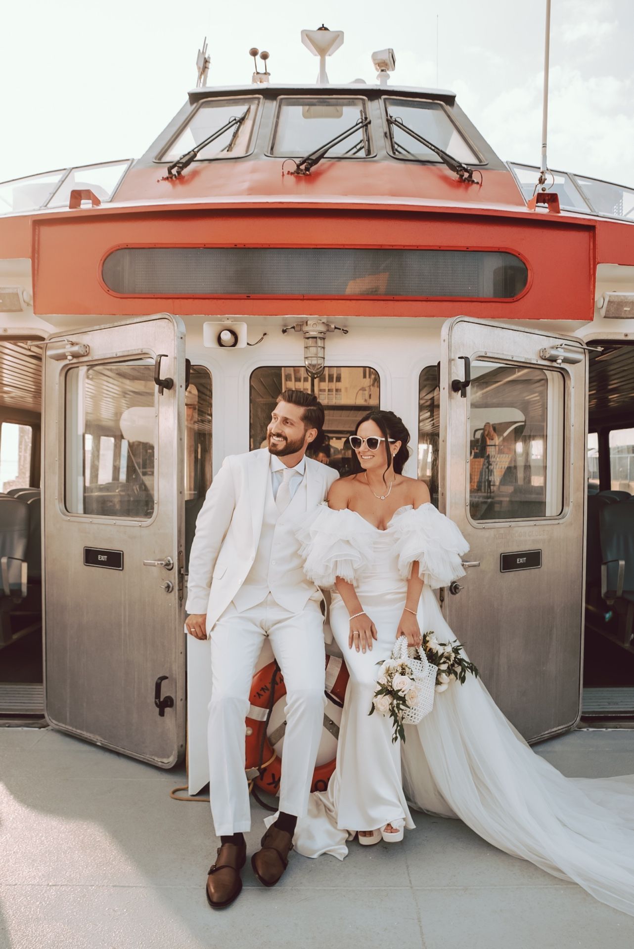 Elegant bride and groom in white posing in front of a red and white ferry boat on their wedding day.