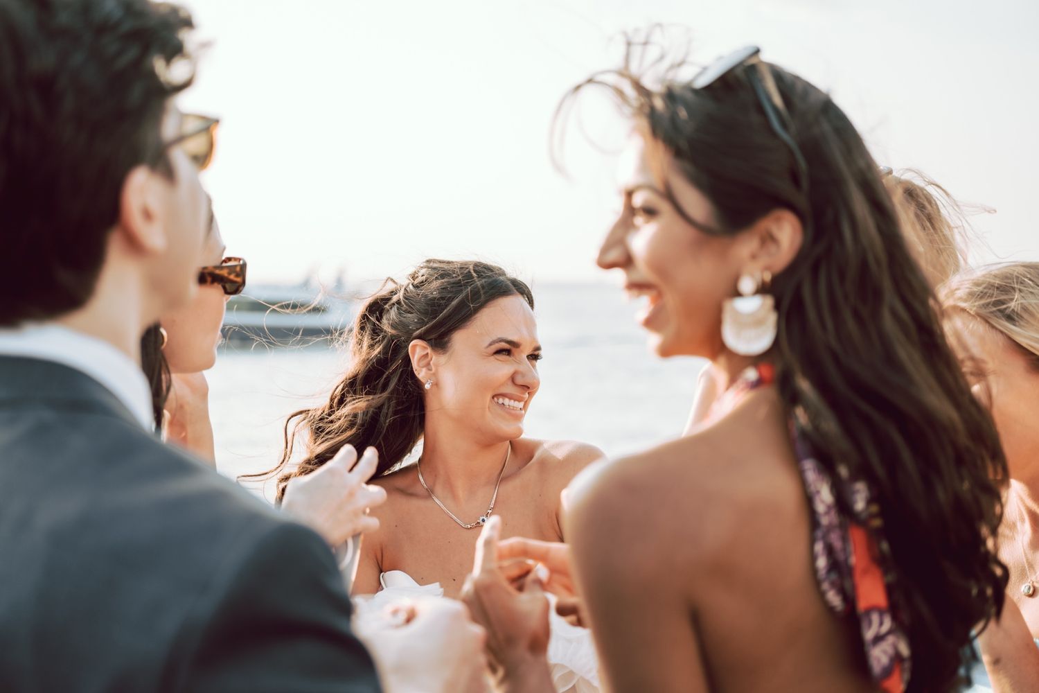 Bride smiling joyfully with guests at an outdoor waterfront wedding celebration.