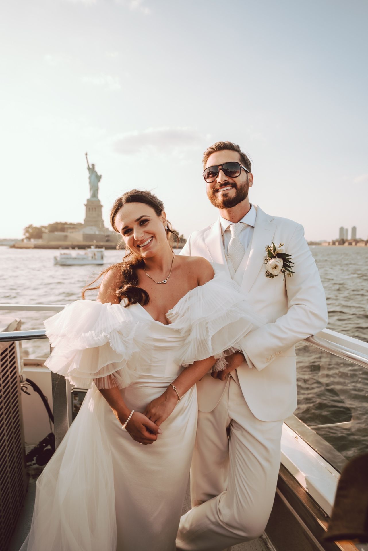 Bride and groom posing on a boat with the Statue of Liberty in the background on their wedding day.