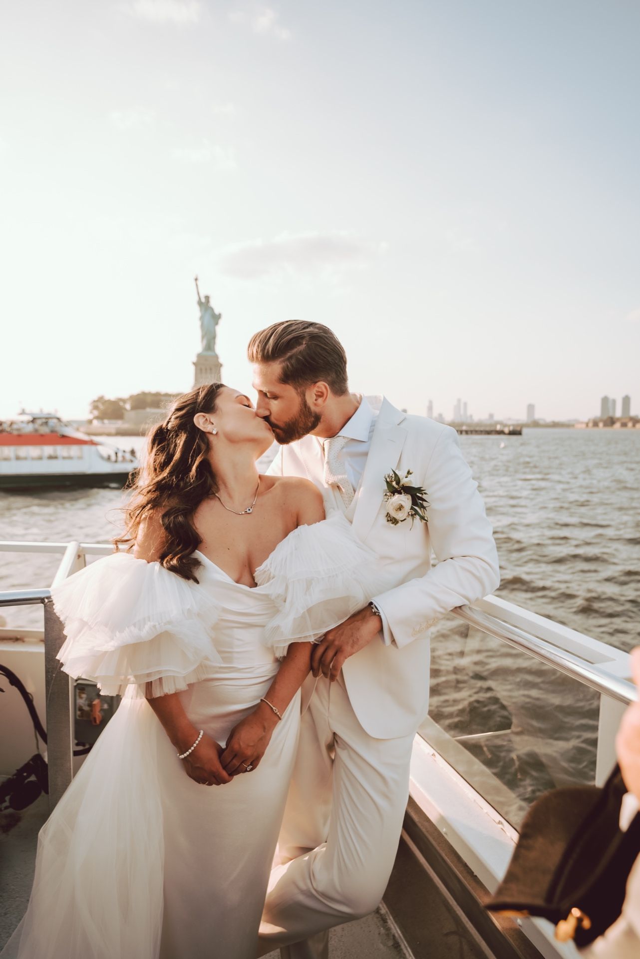 Bride and groom kissing on a boat with the Statue of Liberty in the background.