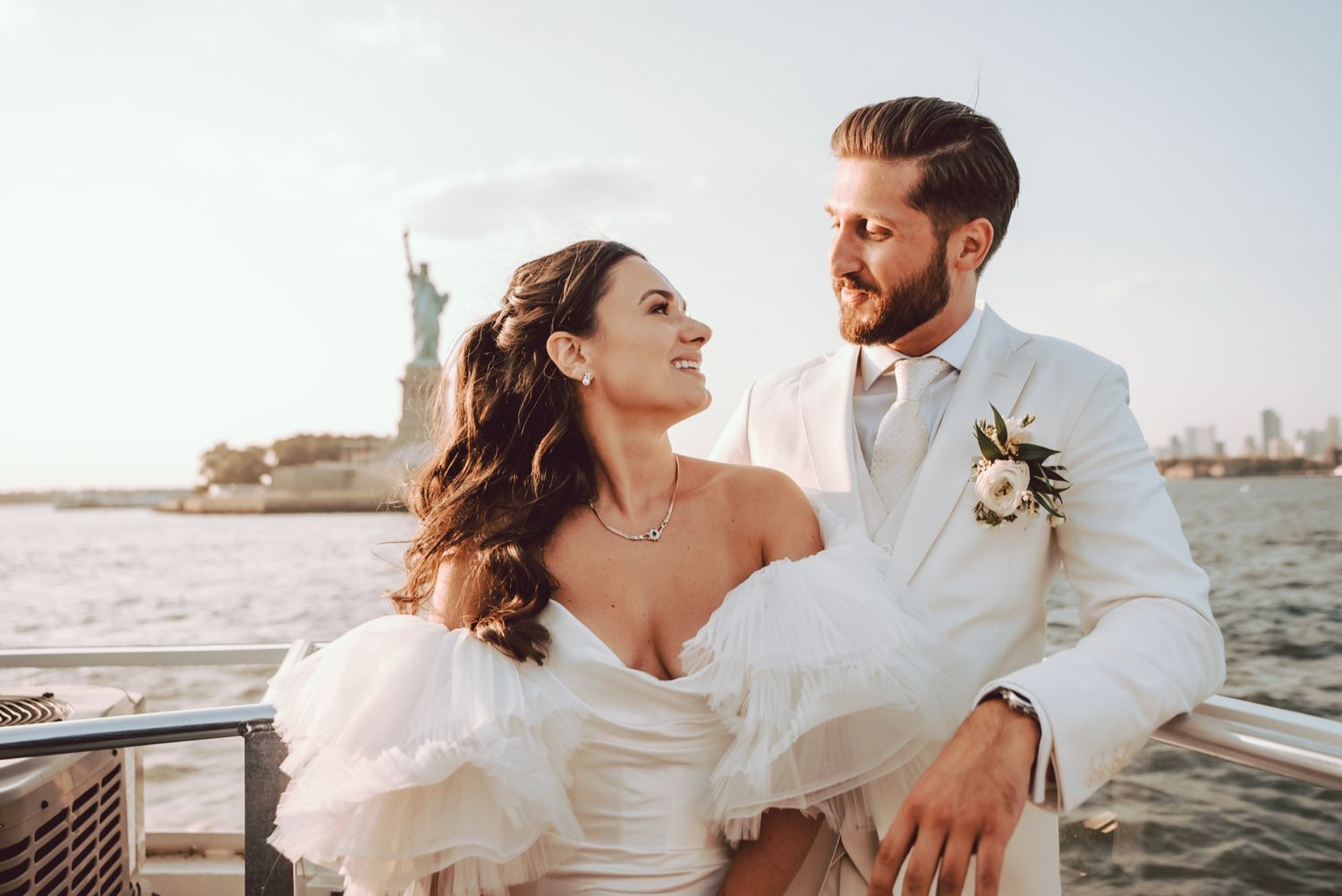 Bride and groom share a romantic moment on a boat with the Statue of Liberty in the background.