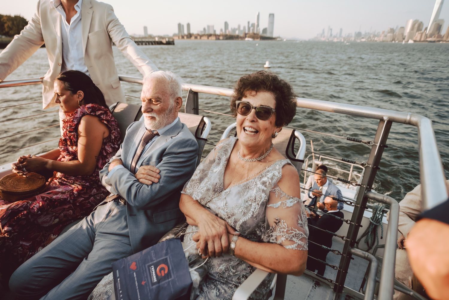 Elderly couple smiling on a boat wedding cruise with city skyline in background.
