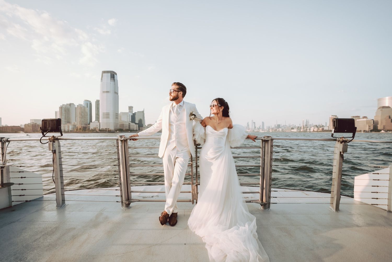 Bride and groom pose on a boat deck with city skyline views on their wedding day.