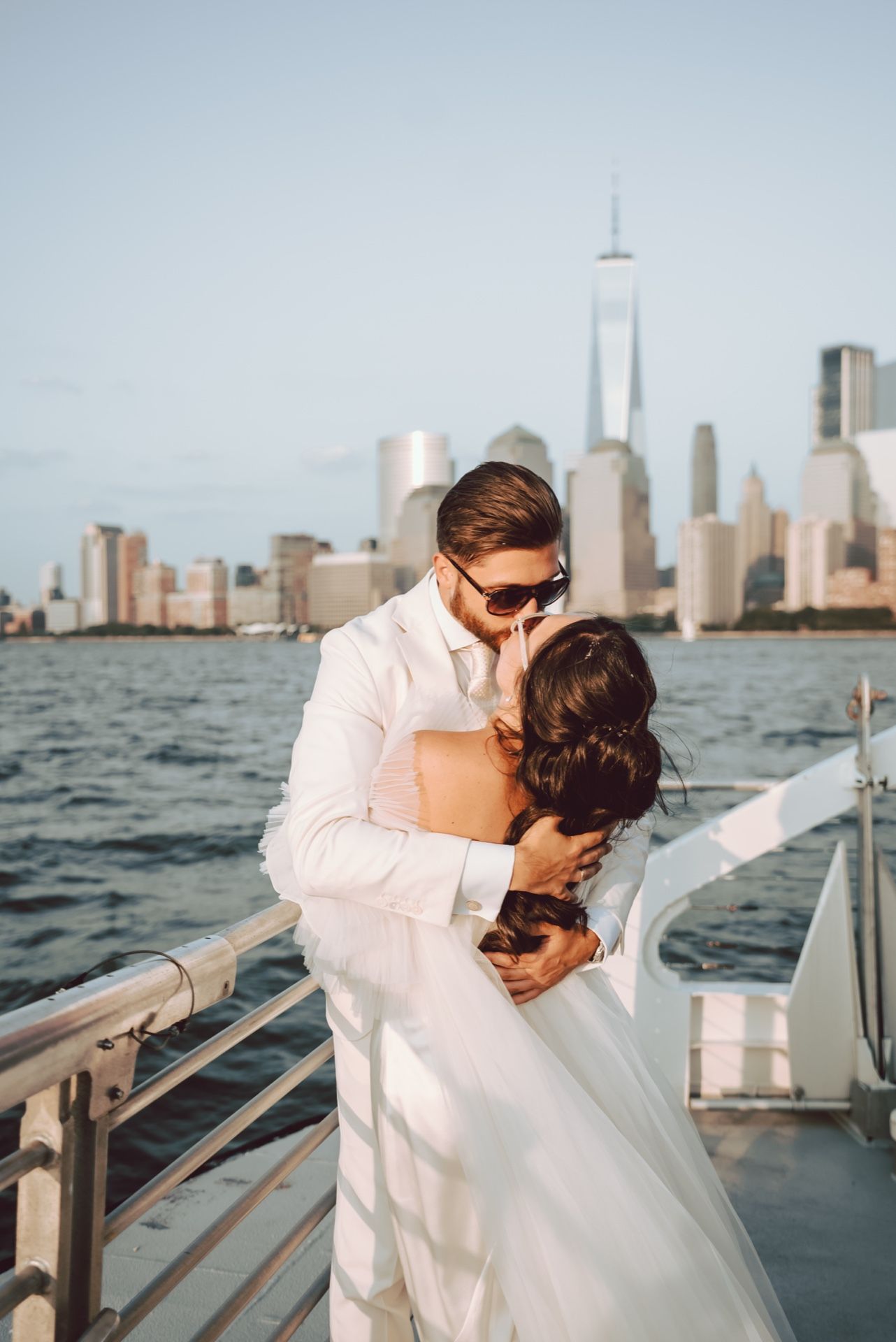 Bride and groom embracing on a boat with NYC skyline and One World Trade Center in the background.