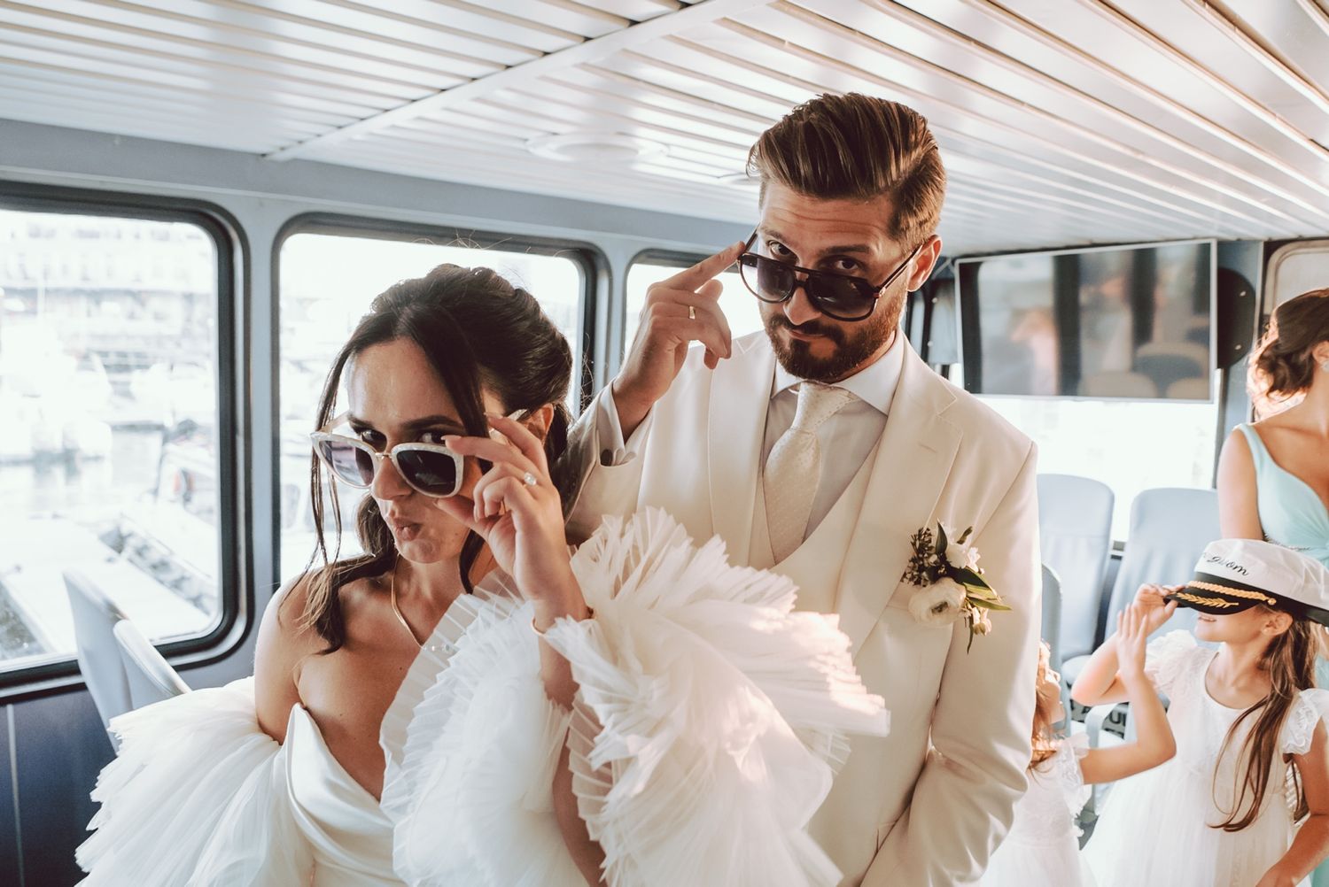 Bride and groom putting on sunglasses together inside a boat at their wedding.
