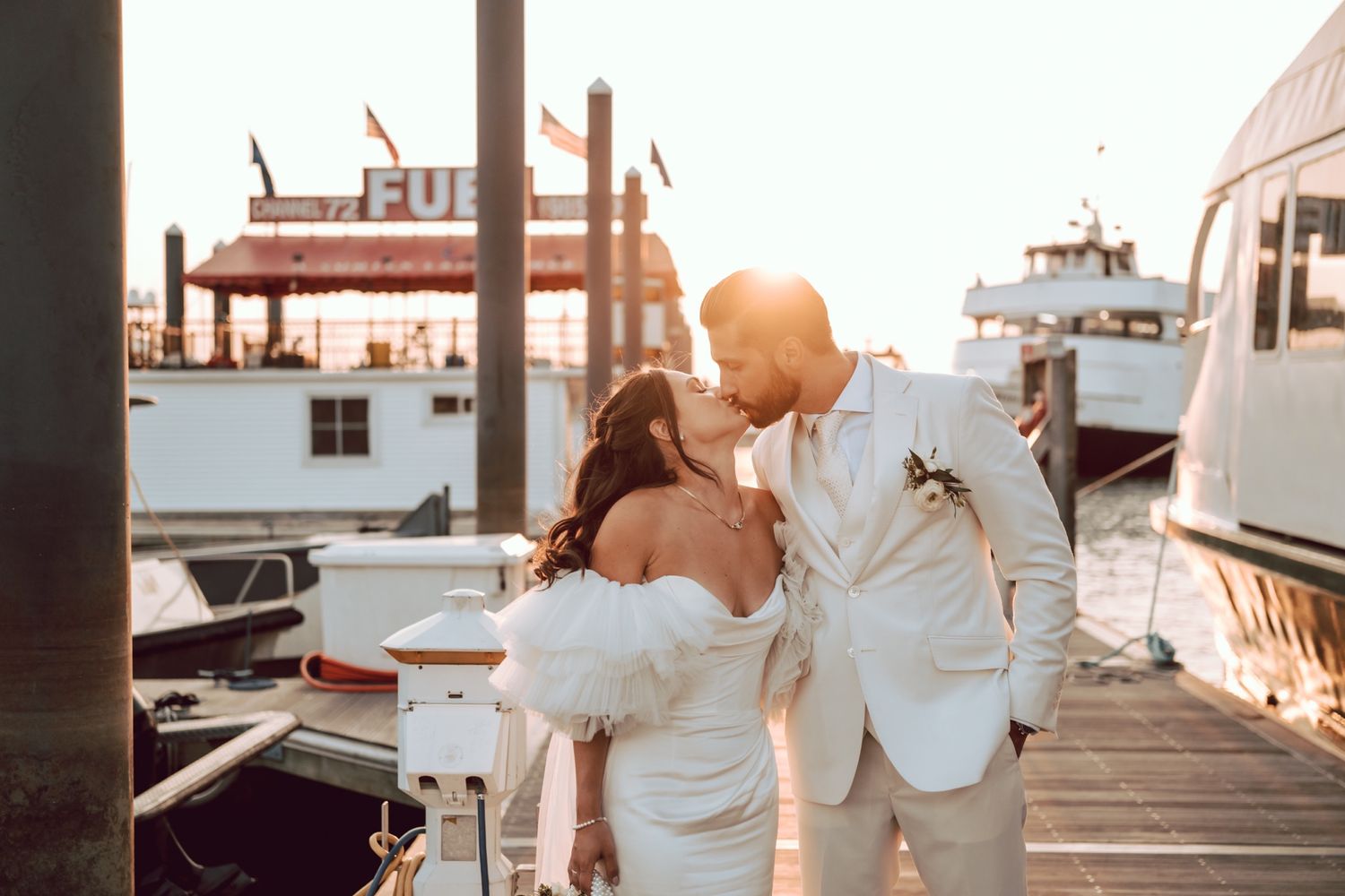 Bride and groom sharing a kiss at golden hour on a marina dock at sunset.