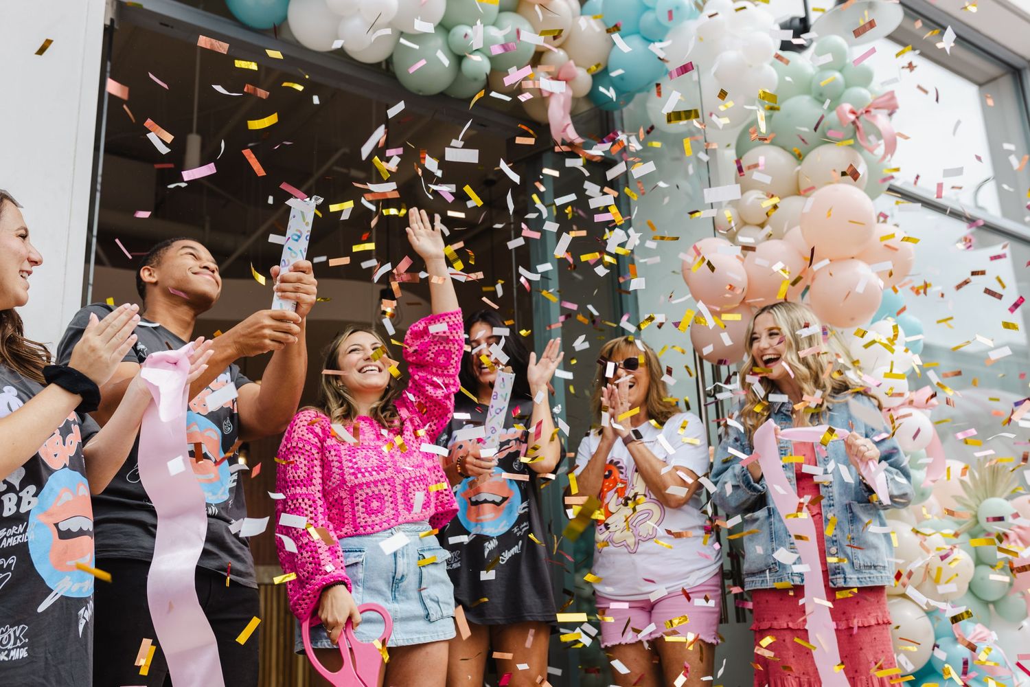 Group of diverse friends celebrating with colorful confetti cannons and balloons at a festive outdoor event.