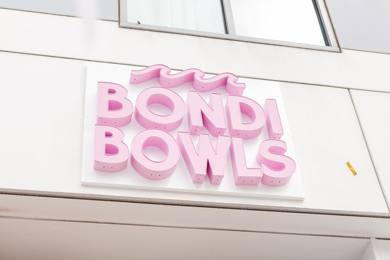 Pink 3D Bondi Bowls sign on white building exterior.