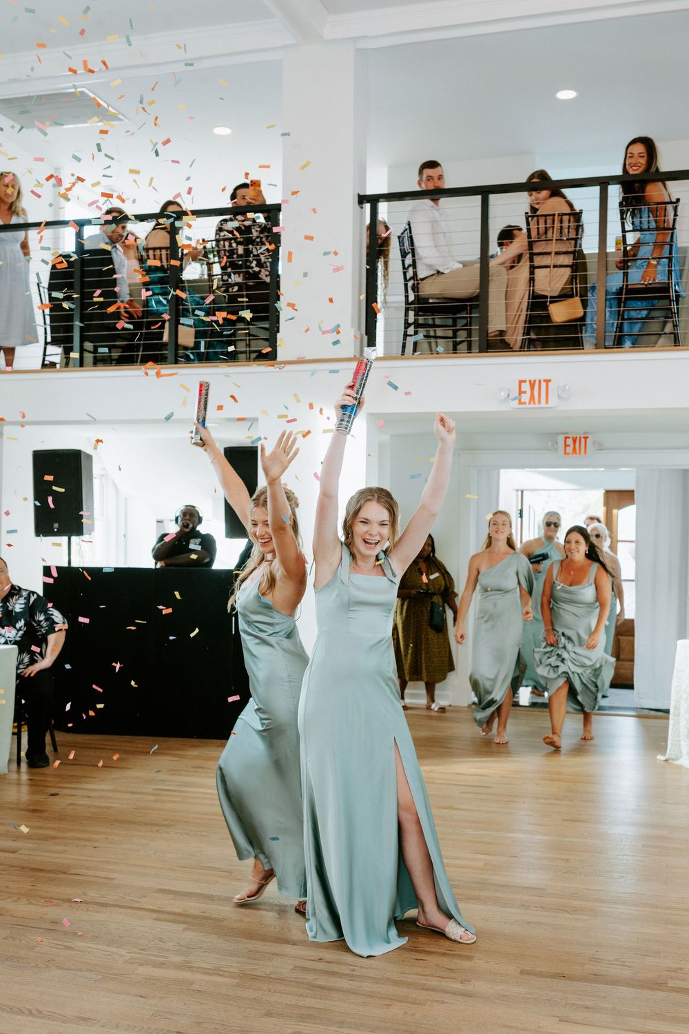 Bridesmaids in sage green gowns celebrate with confetti cannons during a wedding reception entrance.