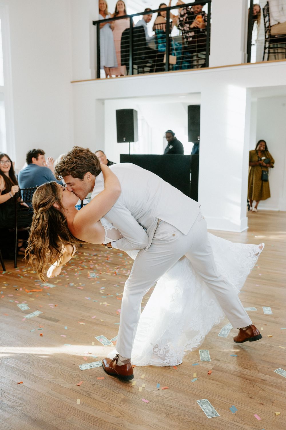 Groom dips bride for romantic kiss on dance floor surrounded by colorful confetti during first dance.