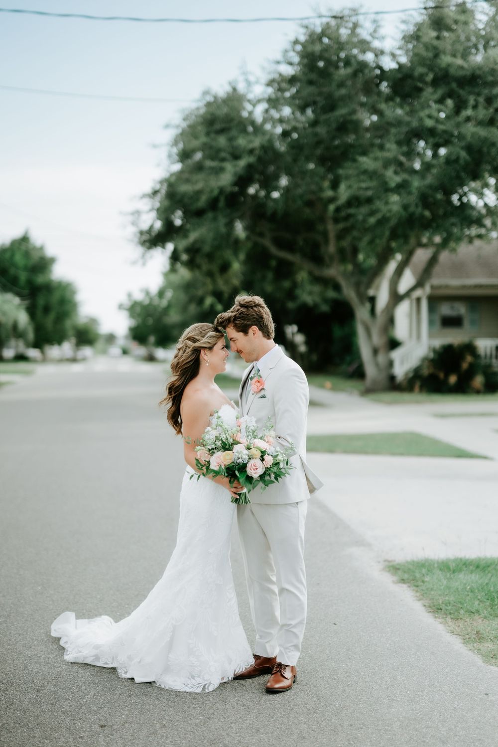 Bride and groom share an intimate moment on a quiet street, bride holding a lush white and pink bouquet.