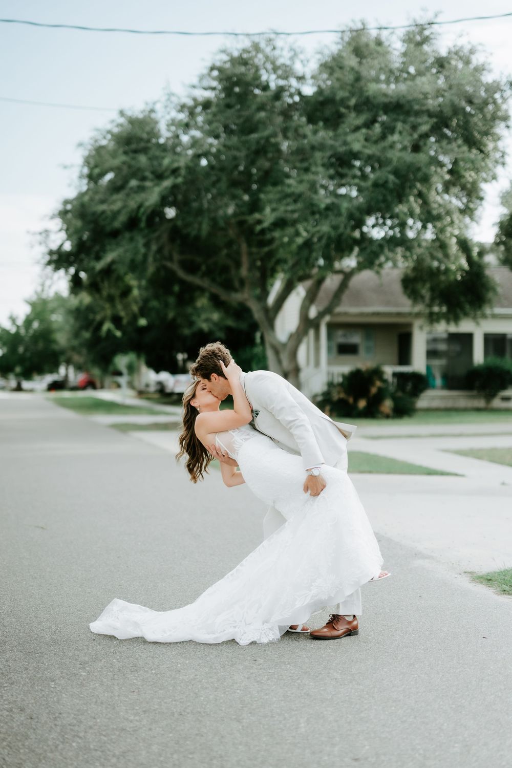 Bride and groom share a romantic dip kiss in the middle of a suburban street in wedding attire.