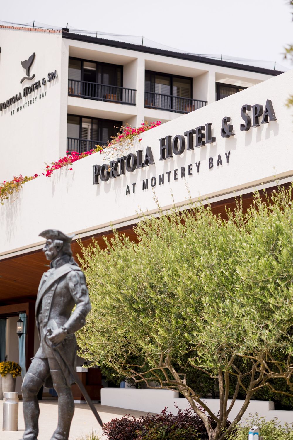 Portola Hotel & Spa at Monterey Bay exterior with statue and lush green trees in foreground.