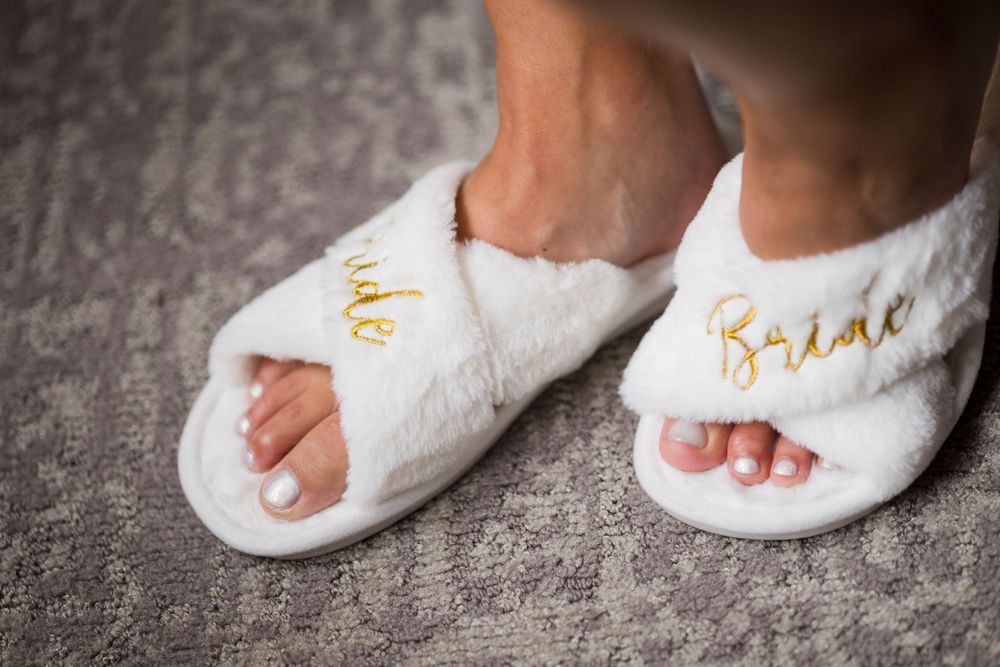 White fluffy bride slippers with gold embroidery worn by a bride on her wedding day.