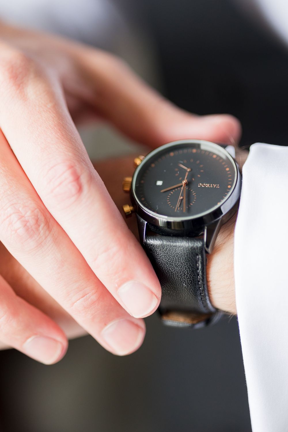 Close-up of a man adjusting a luxury black dial chronograph watch with leather strap on his wrist.