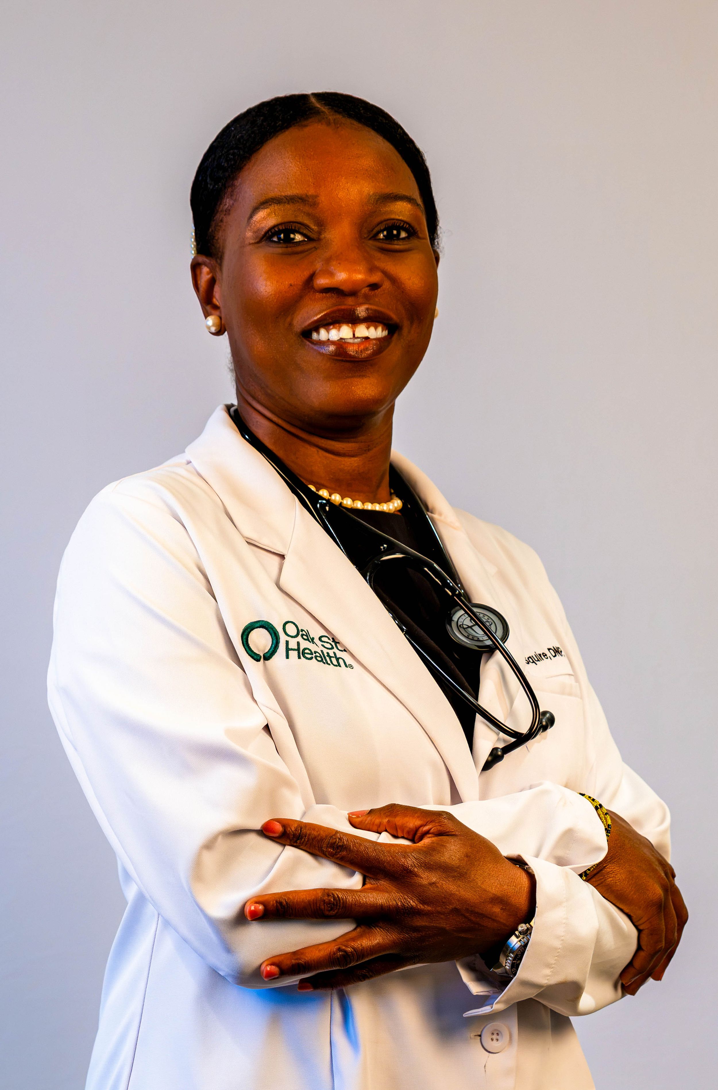 Female doctor in white lab coat with stethoscope smiles confidently with arms crossed at Oak Street Health.