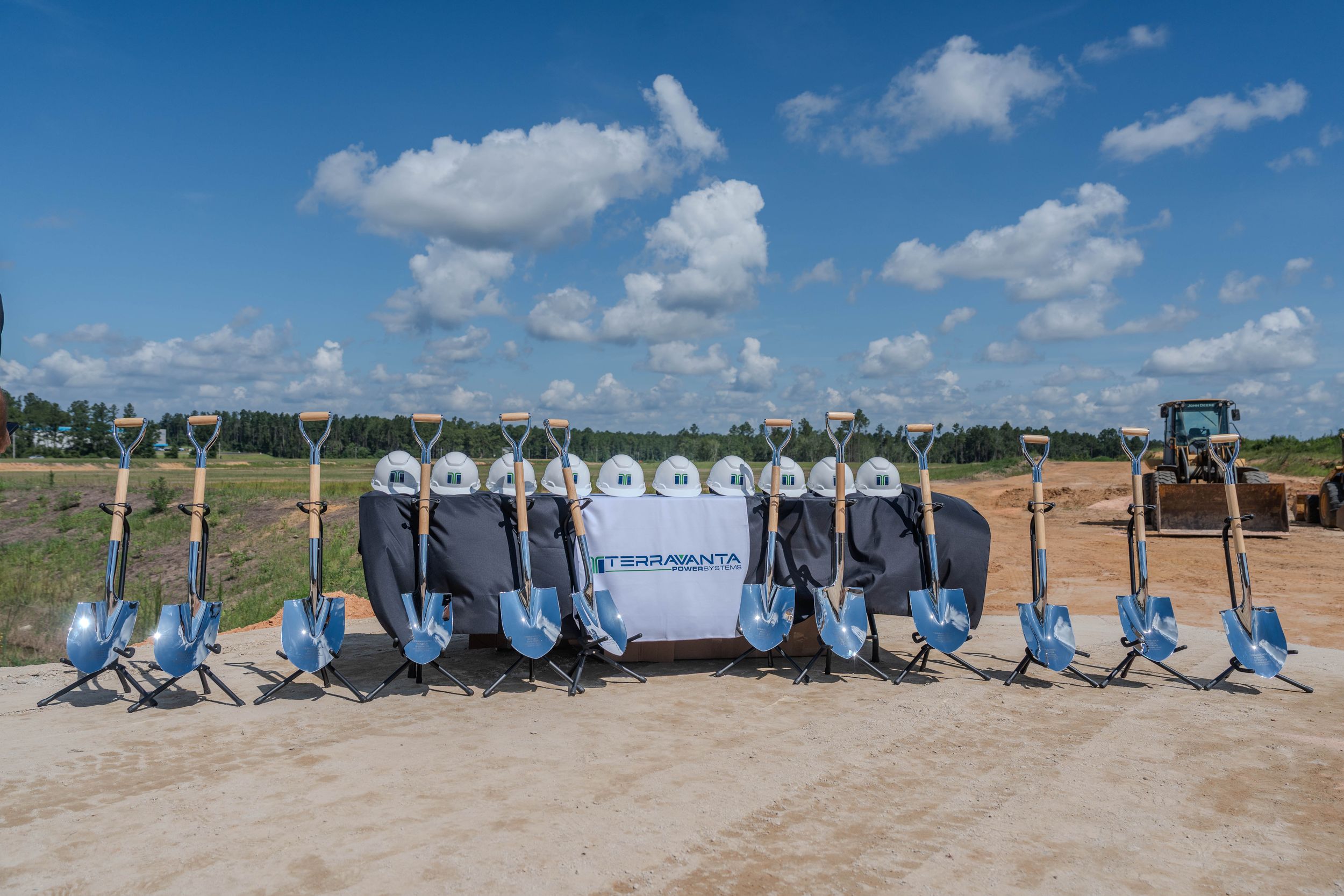 Groundbreaking ceremony with shovels and hard hats displayed on a construction site under a blue sky.