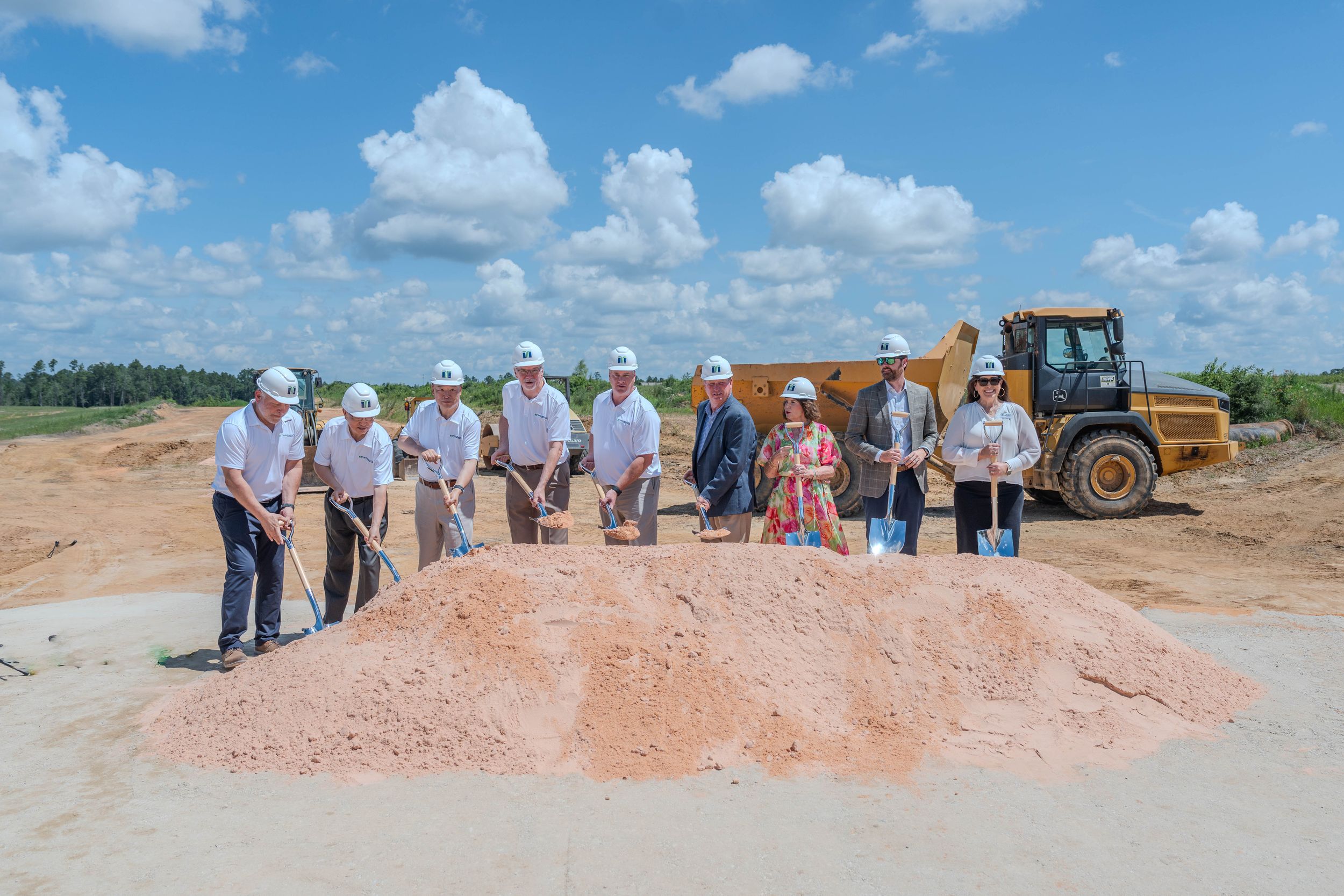 Group of executives in hard hats ceremonially breaking ground with shovels at a new construction site.