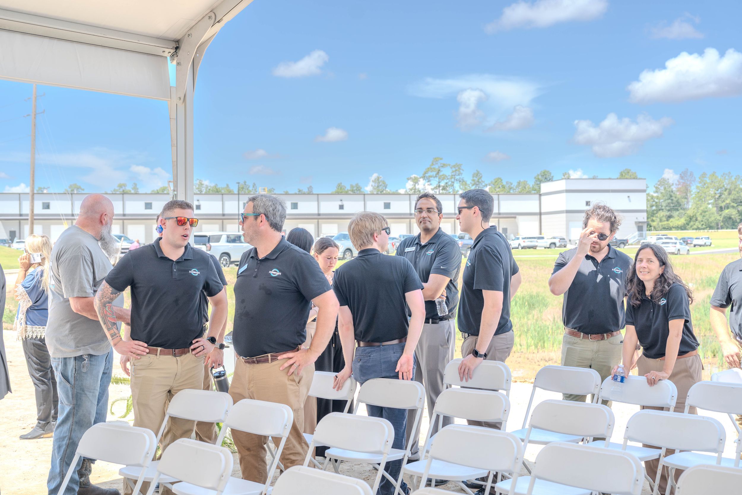 Group of professionals in matching black polo shirts networking outdoors at a corporate event with white folding chairs.