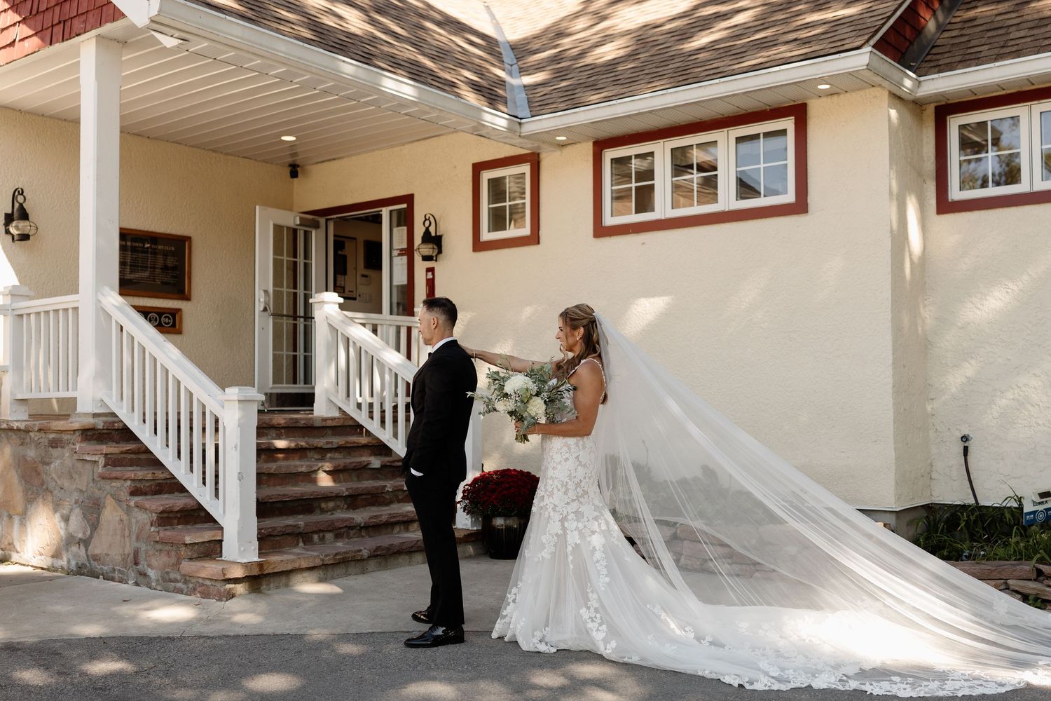 Bride and groom share first look moment outside elegant venue with white staircase and flowing cathedral veil.