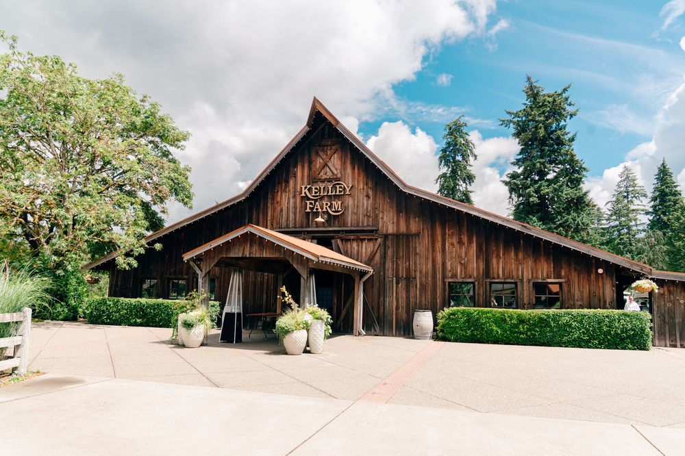 Rustic wooden barn venue surrounded by lush greenery and manicured hedges on a sunny day.
