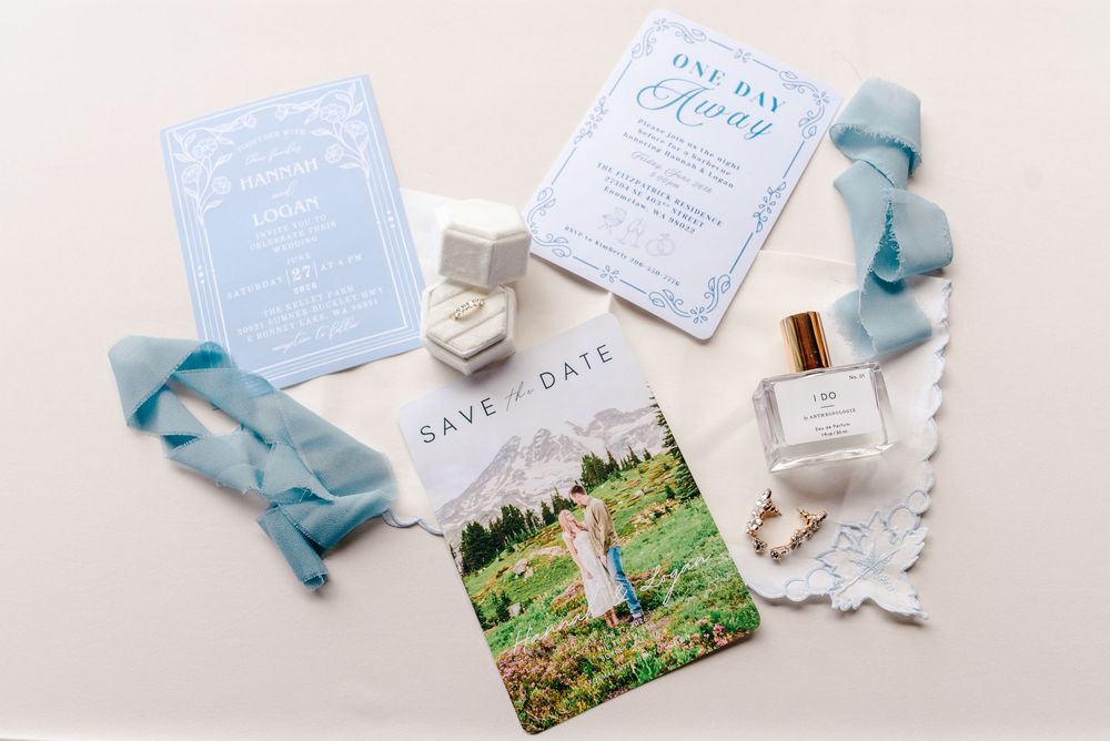 Elegant wedding stationery flat lay with blue invitations, save the date card, ring box, perfume bottle, and silk ribbon.