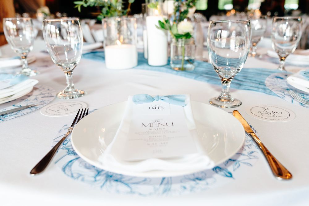 Elegant wedding table setting with blue marbled tablecloth, crystal glasses, gold cutlery, and a white menu card on a plate.