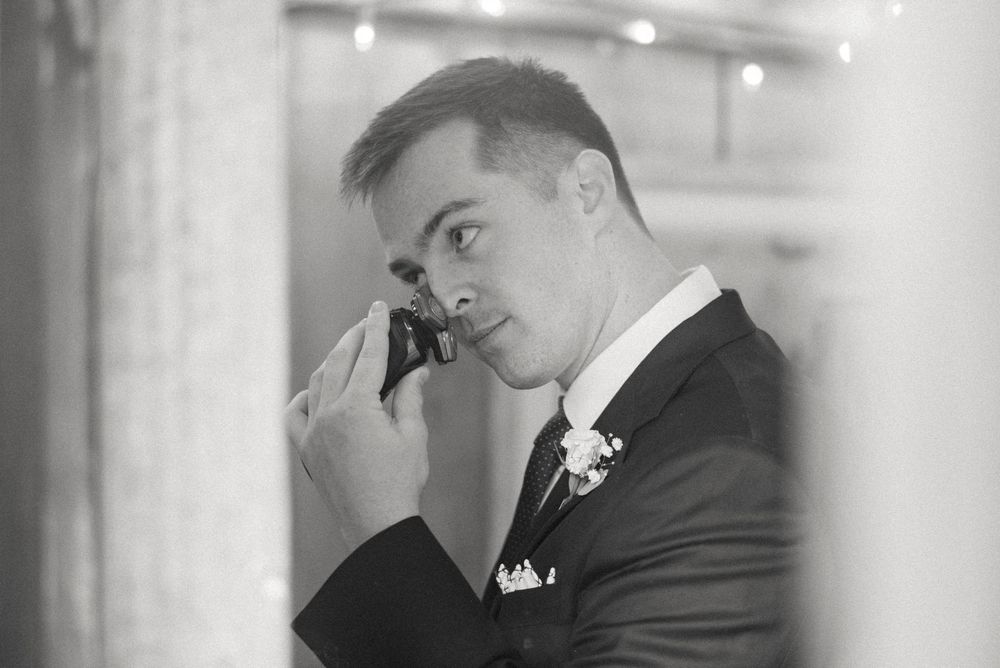 Black and white photo of an emotional groom in a suit wiping tears at his wedding ceremony.