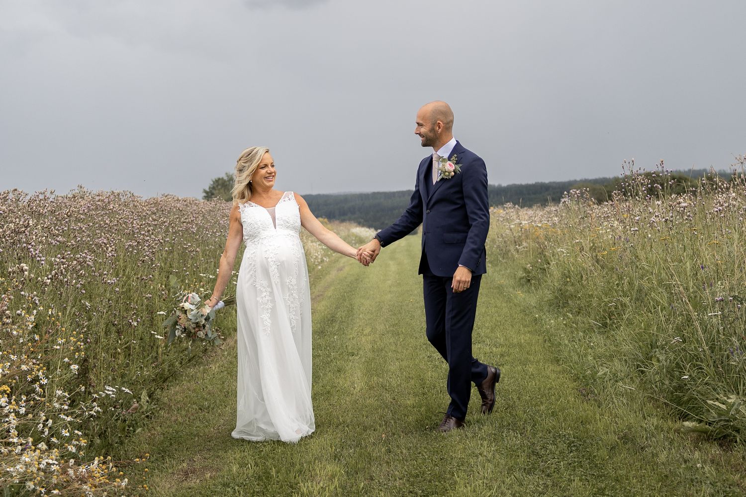 Brudpar håller varandra i handen på en blommande äng under sin bröllopsdag
