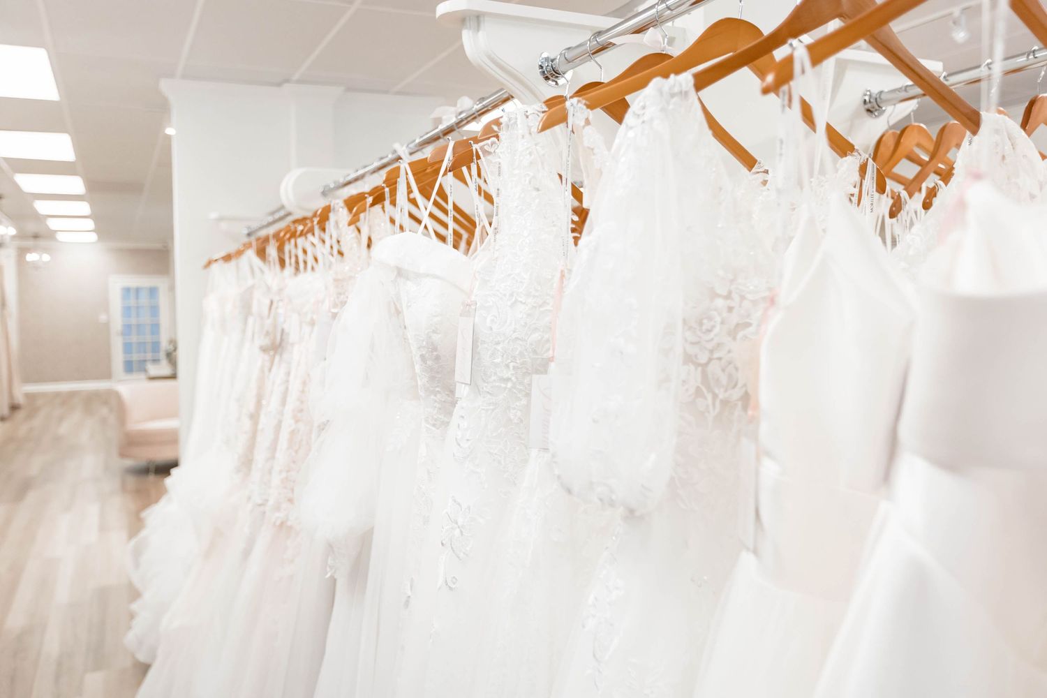 A row of elegant white wedding dresses on wooden hangers displayed in a bridal boutique shop.