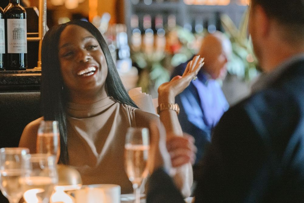 A woman laughing and gesturing during a dinner date at an upscale restaurant with champagne glasses on the table.