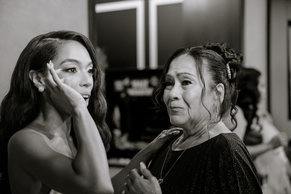 Black and white photo of two women, one applying makeup to the other, in an elegant getting-ready scene.