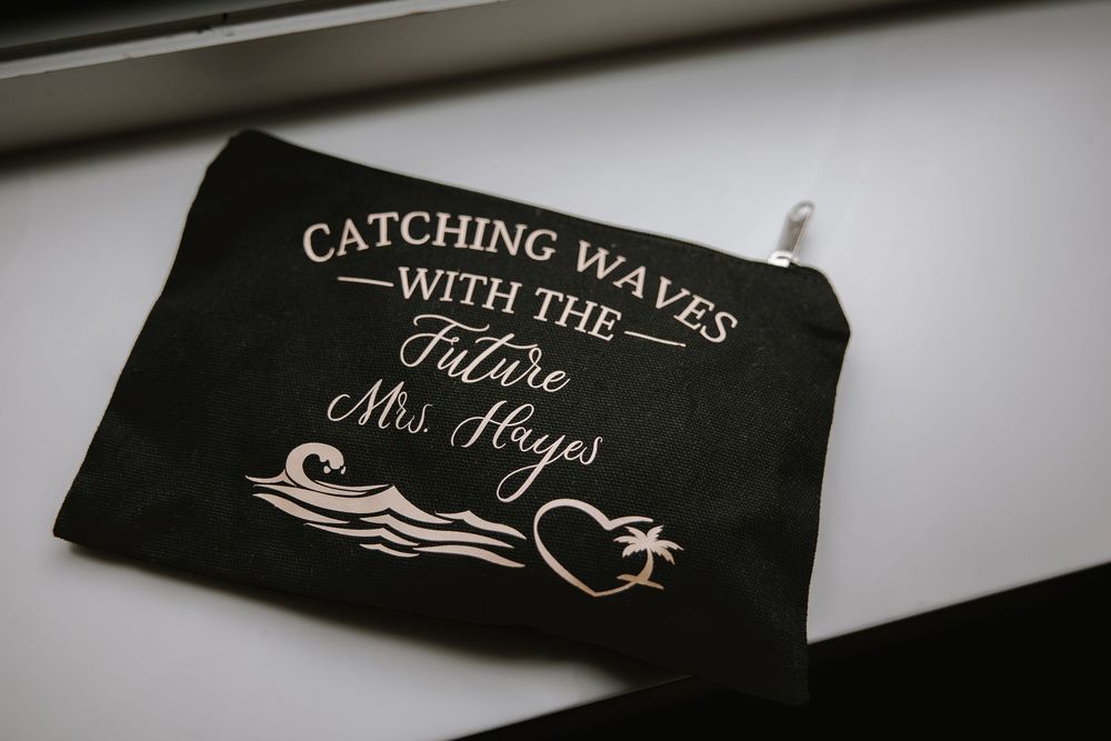 Black canvas zipper pouch with rose gold text reading Catching Waves With The Future Mrs. Hayes with wave and heart design.