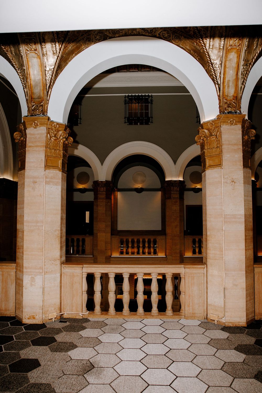 Ornate golden arched colonnade with hexagonal tile floor in a grand historic building interior.