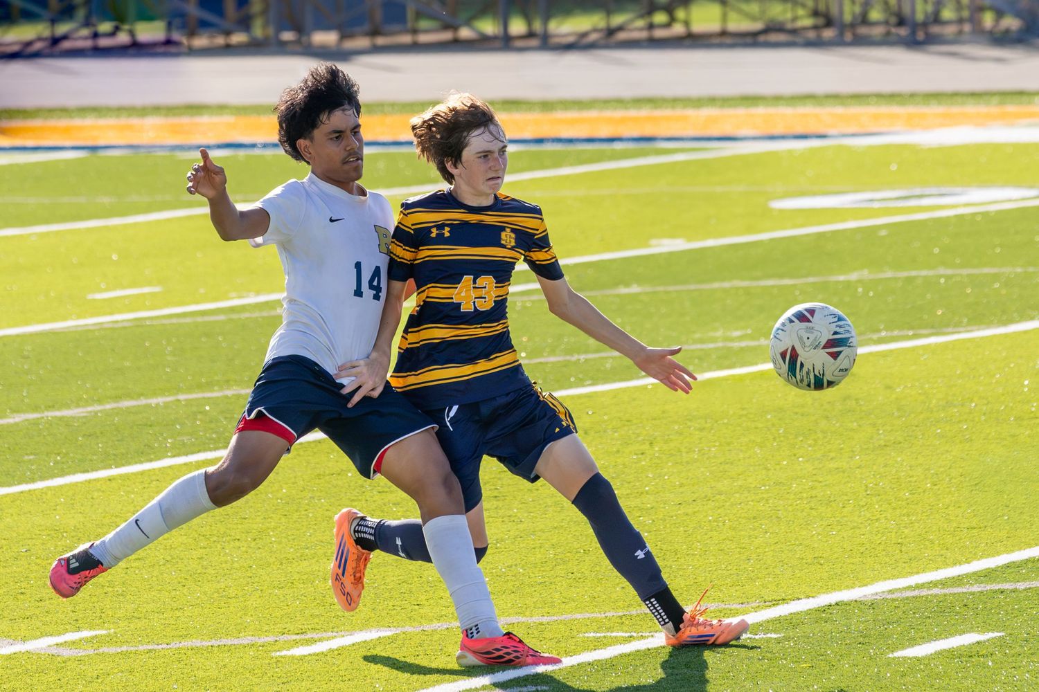 Two male soccer players compete for the ball during a match on a green turf field.